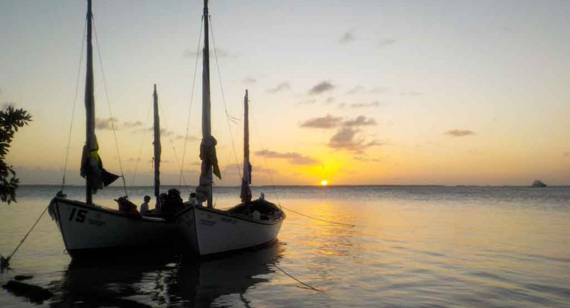 two sailboats rest on calm water at sunset